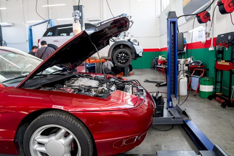 Red car with open hood in auto repair shop with lift and tools visible